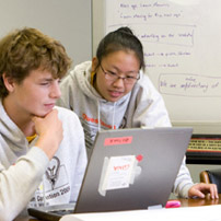 A young man and woman looking at the screen of a laptop computer.