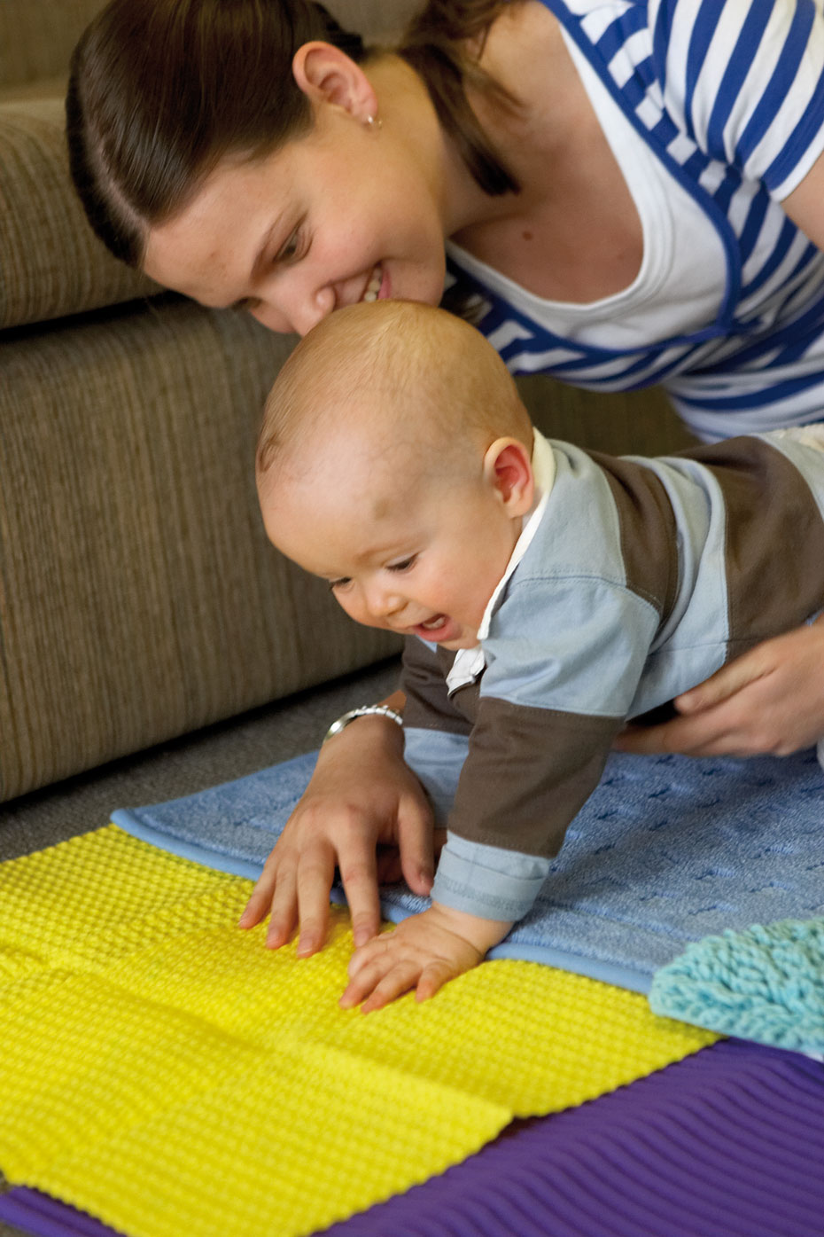Babies learn through all their senses, including touch. A woman and a baby on the floor looking at a yellow piece of material.