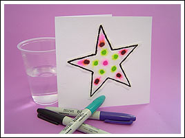 Chromatography is a method of separating the parts of a mixture. A white card standing upright with a pink-and-green spotted star on the front. A plastic cup is sitting next to the card, and three coloured markers are sitting in front.