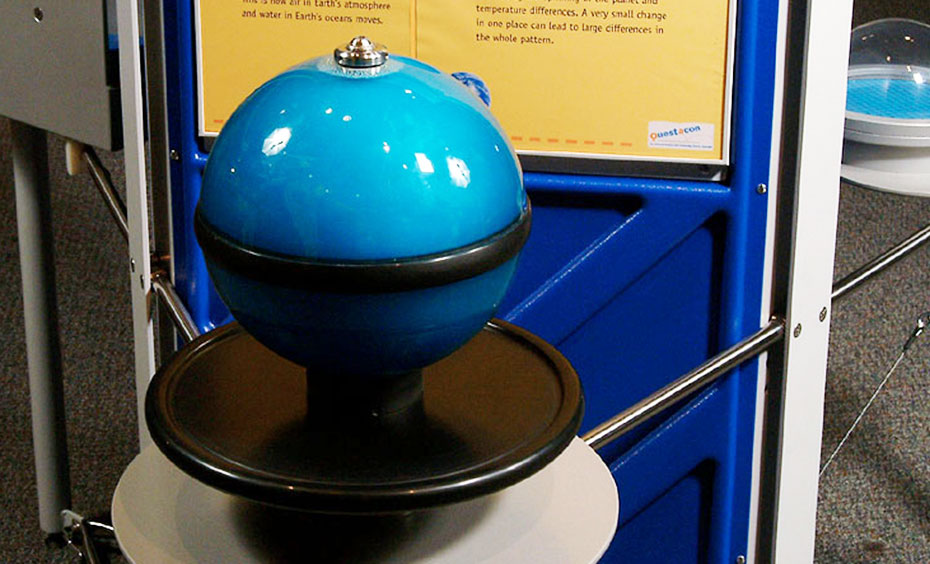 Spin the sphere slowly, then quickly and compare different patterns in the fluid. A exhibit with a blue and black sphere at the front and a yellow and blue information panel at the rear.