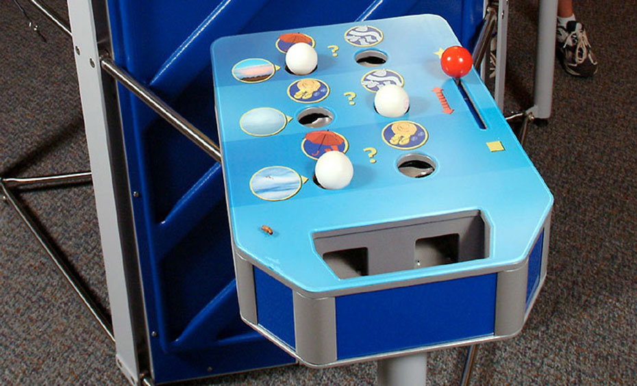 Look at the cloud photographs, think about the weather each cloud may bring and place a ball in a spot that represents clothing best suited to your weather forecast. A blue table that has white balls, holes and a red lever in the top.