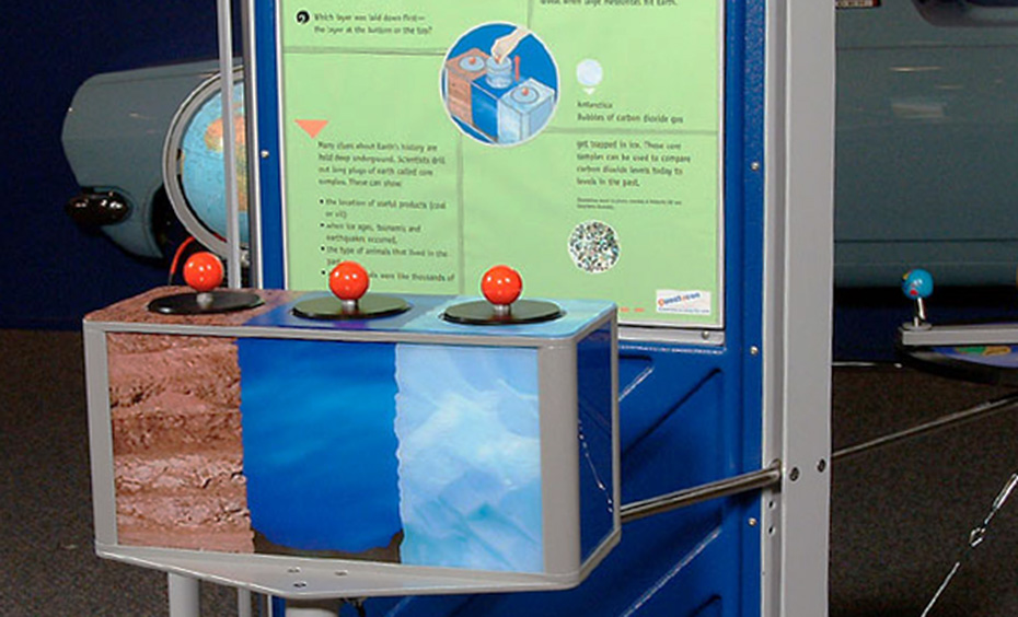 Lift each knob to look at the model core samples (not to scale). A blue, green and grey exhibt which has 3 core sample boxes at the front with red knobs on top of each, and a large vertical information panel at the back.