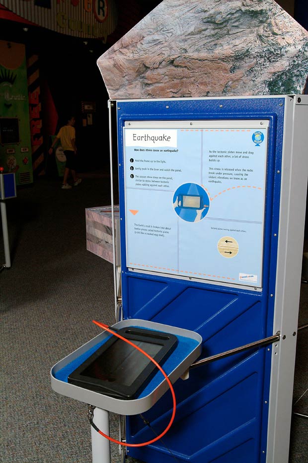 Earthquakes occur due to energy released from compressed rocks. A black frame filter sitting on a blue and grey tray, is in front of a blue and white vertical information panel.