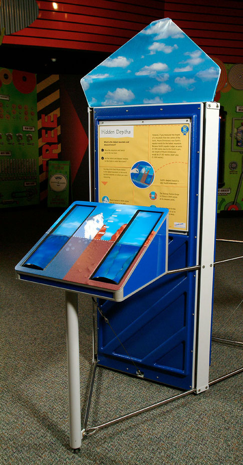The tallest mountain and deepest trench on Earth can be found (partially or fully) under the oceans. A yellow, blue and brown exhibit that has a triangular prism at the front and a large veritical information panel at the back.