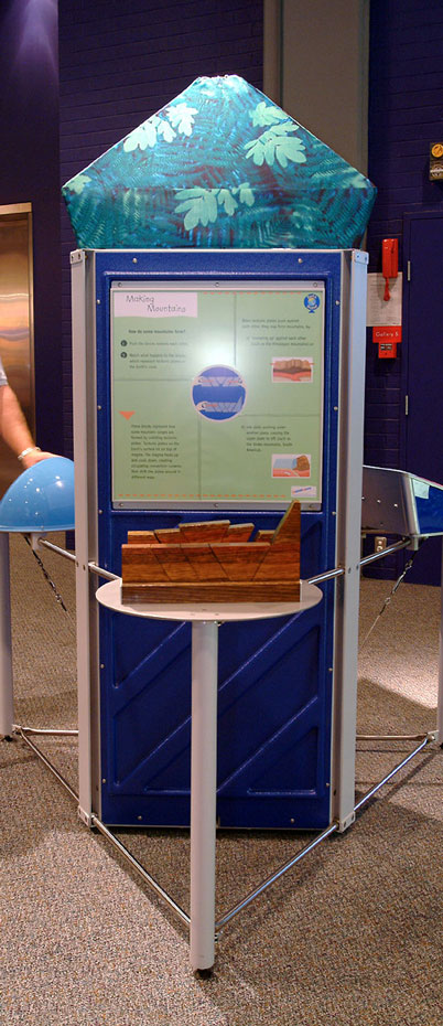 Mountains form when tectonic plates move against or above each other. A blue, green and grey exhibit stand with a large piece of timber at the front with slots cut into it.