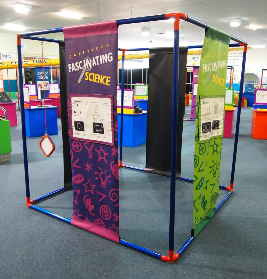 Follow graphic panel instructions about reading text while performing certain actions. A large blue and red cube frame that has purple and green information banners hanging between top and bottom bars of the cube.