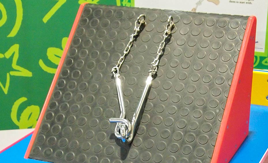 Untangle the metal hoops using logical thinking skills rather than brute force! Two stainless steel hoops attached by chains to a black and red triangular prism.