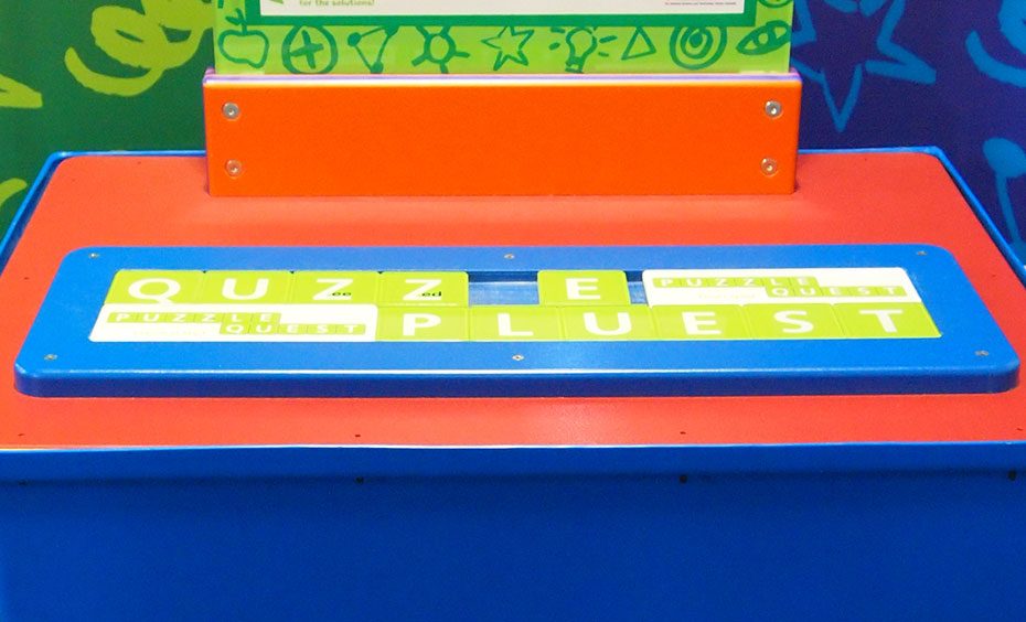 Slide puzzle pieces around to swap the 'Zed' and 'Zee' tiles. On a blue and orange surface sits a flat green and white word puzzle, set in a blue frame.