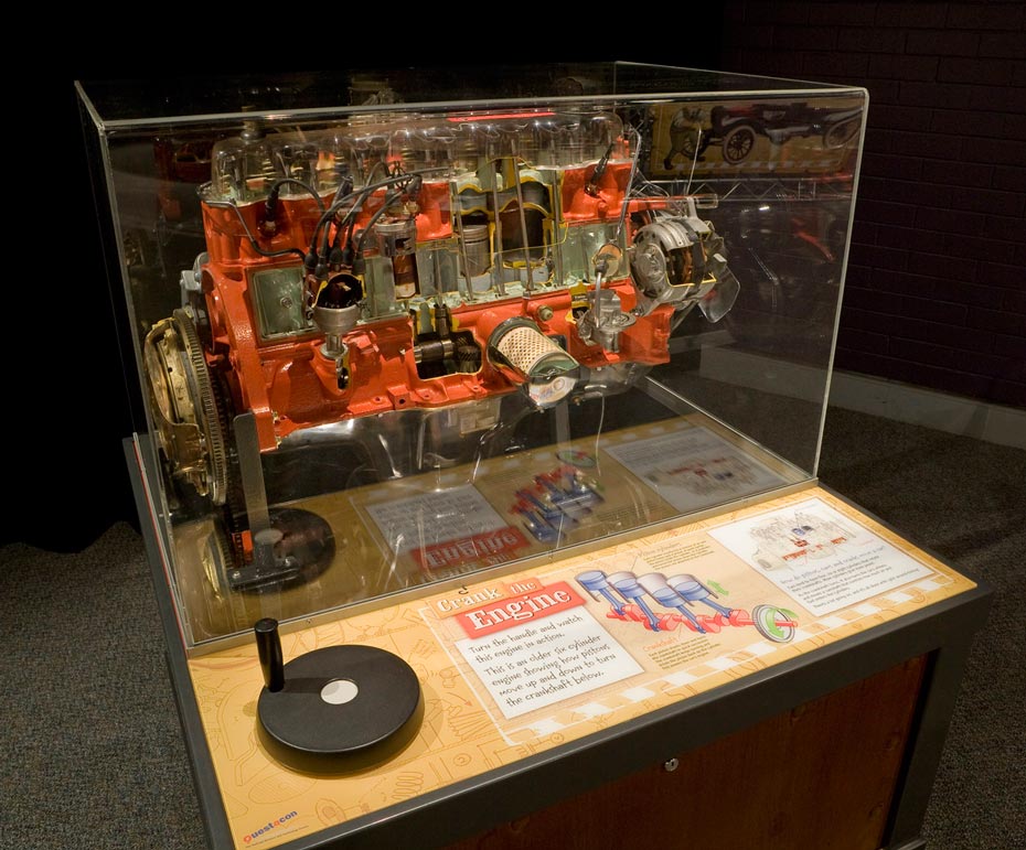 Pistons and crankshafts within car engines interact to create movement in a car. A full scale petrol combustable engine with cut away areas, showing the cylinders and pistons, all encased in a perspex box.