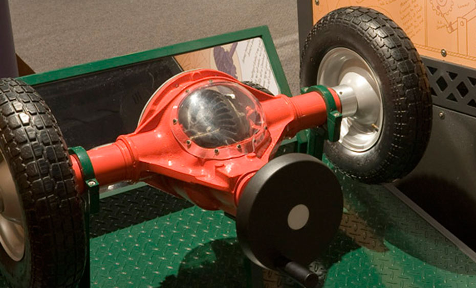 Turn a handle and observe how separate gears and axles turn car wheels at different speeds. Try holding one wheel still and keep turning the handle to observe how the second wheel responds. A black and green display base that has a red, car differential with a see-through window to show the gears.