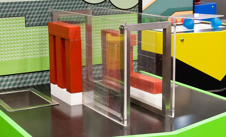 Is there a pattern in how far each block overhangs its block underneath? A black, green and grey exhibit table with vertical information panel and a series of red and white blocks on the table surface.