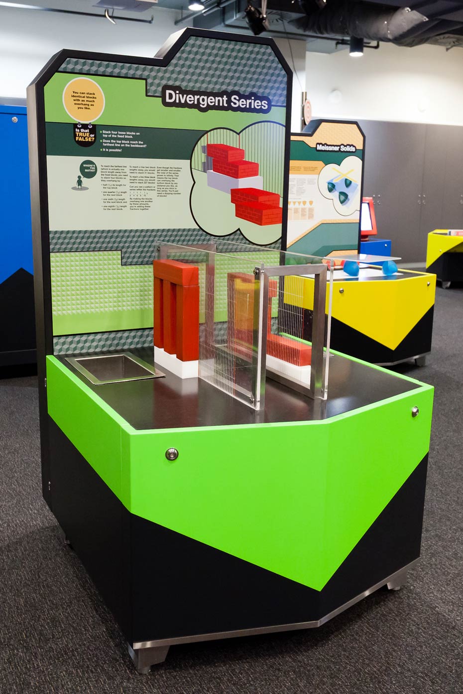 Not all series explode to infinity. Some get closer and closer (they converge) to a number. A black, green and grey exhibit table with vertical information panel and a series of red and white blocks on the table surface.