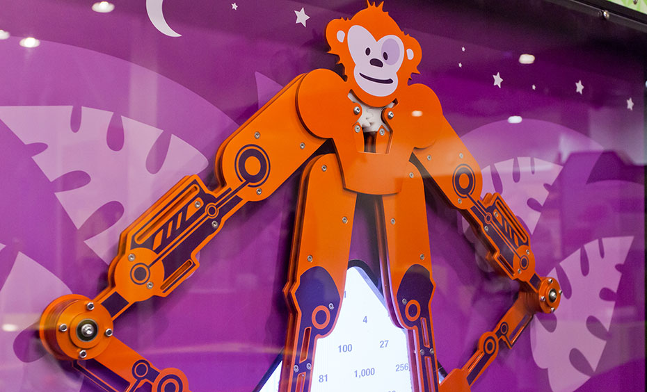 Move the mechanical monkey’s feet to numbers along the baseline and watch the monkey’s hands reveal the answer on the screen to your chosen mathematical operation. An orange mechanical monkey in front of a purple background.