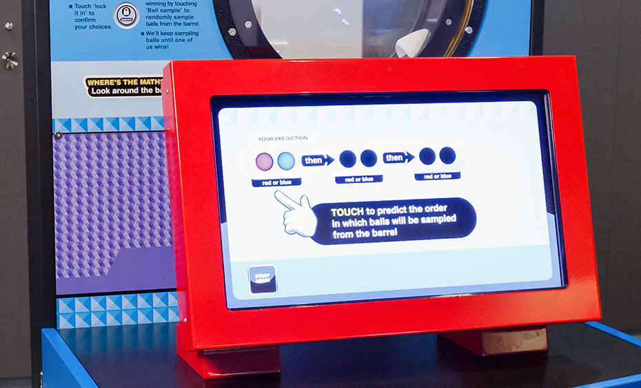 redict via touch screen the order or sequence in which three coloured balls will be sampled from a barrel, then the exhibit's computer will make a sequence prediction and display it on the screen. A blue, black and red exhibiti with a round port hole at the top and a red monitor in front.