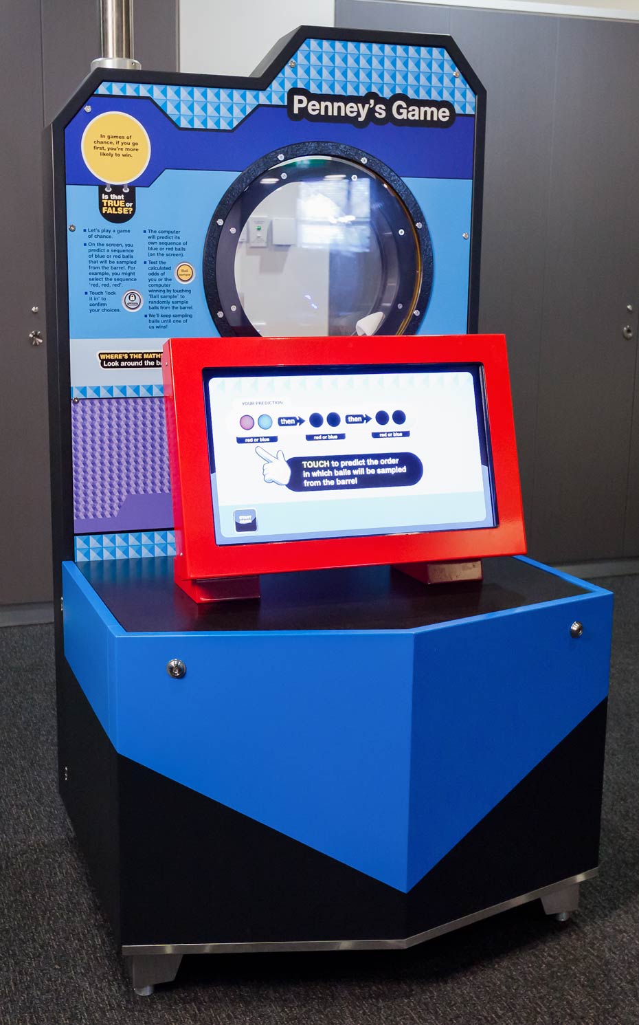 Does it matter whether you go first or second when selecting your predicted sequence of coloured balls? A blue, black and red exhibiti with a round port hole at the top and a red monitor in front.