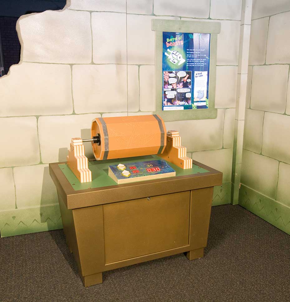 By comparing the ratio of tagged to untagged animals, a reasonably accurate estimate of the total population of animals can be calculated. A fake stone wall in the background with a blue information panel displayed. In the foreground is a brown table with an orange cylinder on top laying on it's side with a steel spindle through it's centre. There are controls in front of this on the top of the table.
