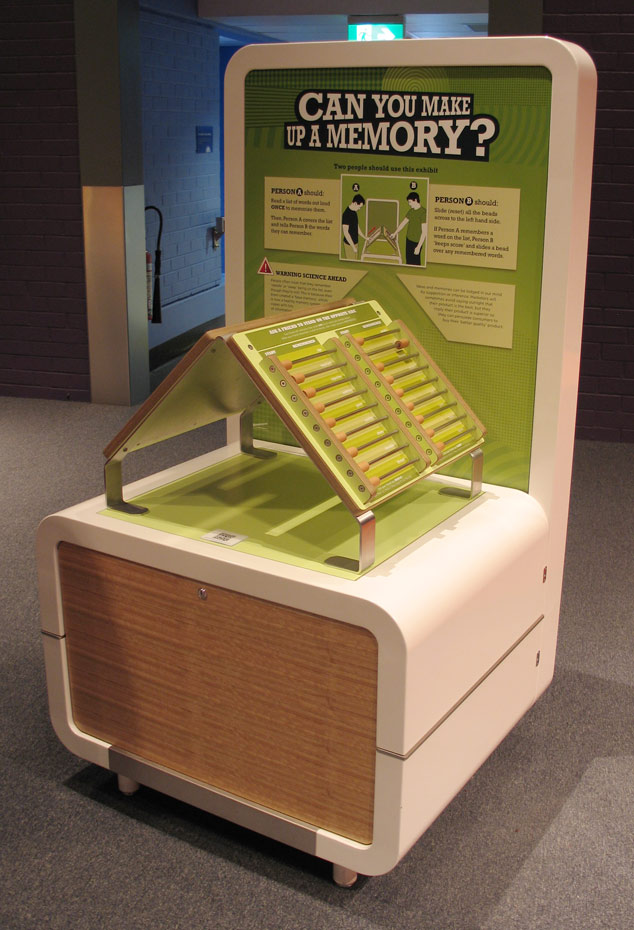 This exhibit needs two people. One person reads out loud a list of words to the second person. A green and cream coloured exhibit table with the words 'can you make up a memory' on it. on the table top are two boards resting at 90 degrees towards each other.