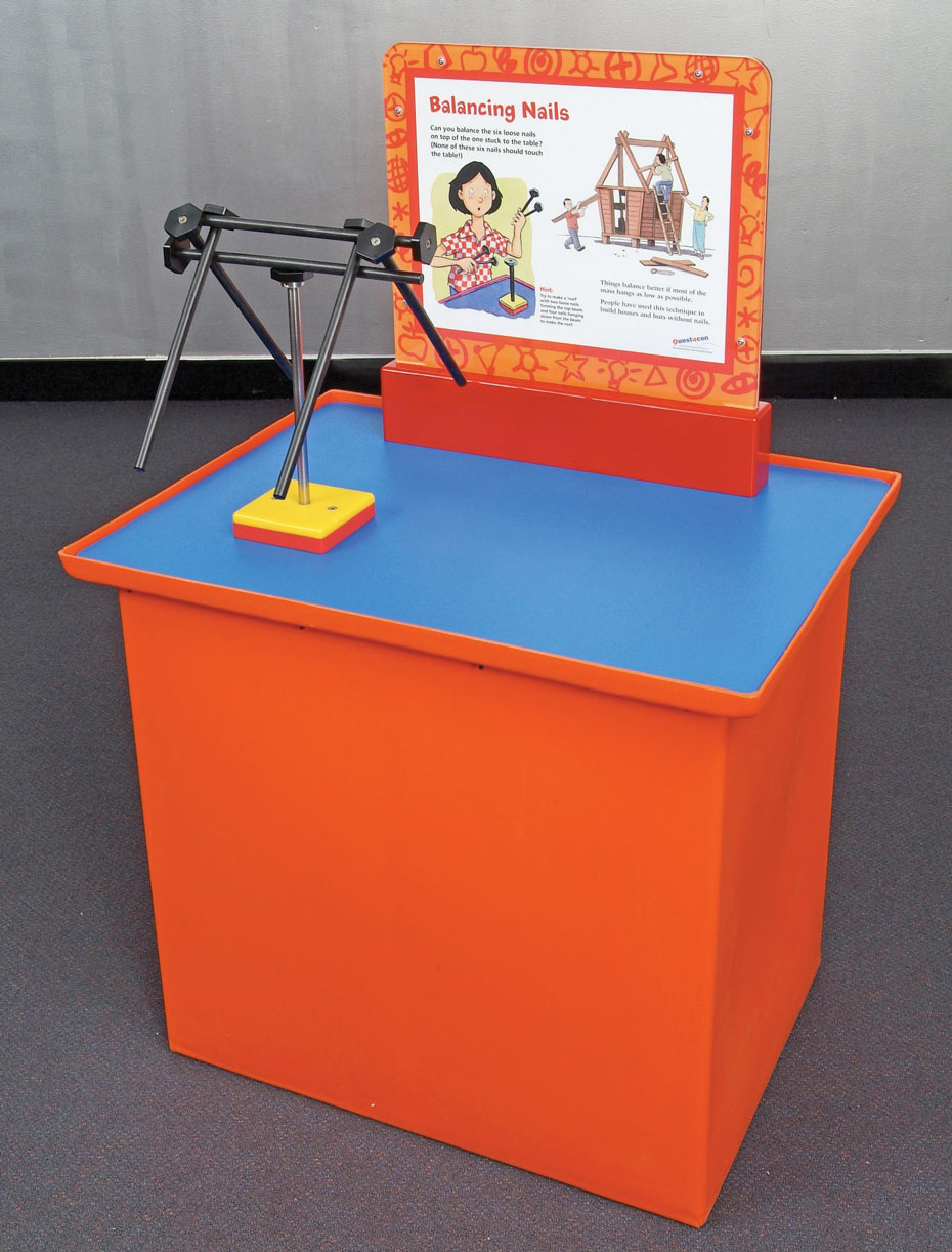 Centre of mass can be used to hang objects together. A orange and blue exhibit table with a matching information panel on top, as well as black steel rods that are balancing amongst one another on a single stand.