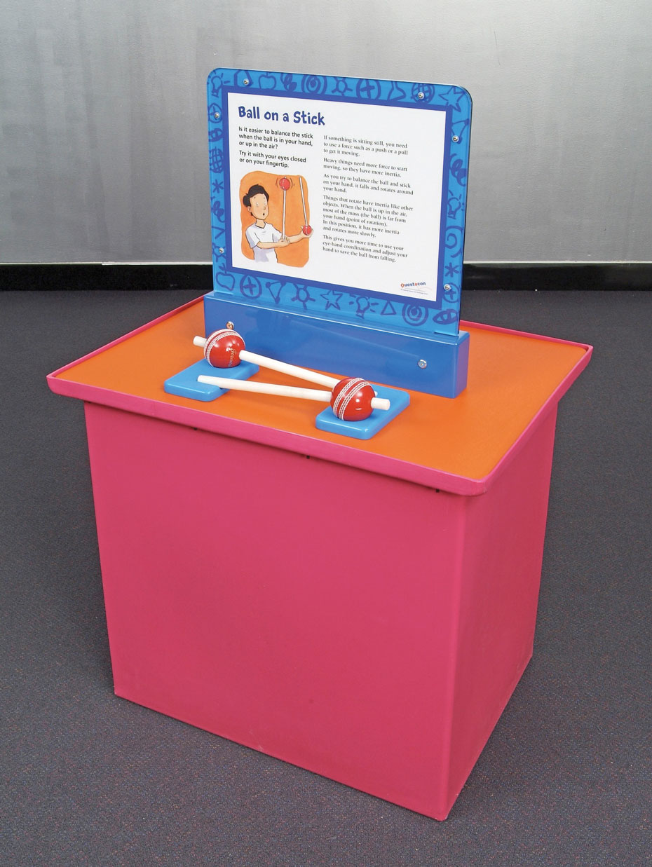 It's easier to control how something moves when the object's mass is far from its turning point. A pink and orange display table with a vertical blue information panel on top. In front of the panel, are two red cricket balls which each have a shite stick going through them.