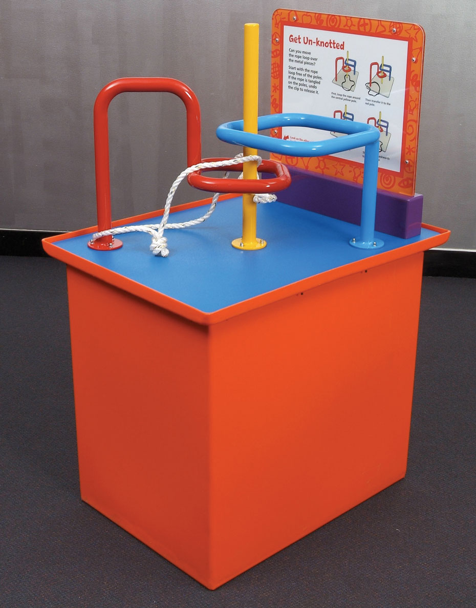 Thread a loop around two interlocking poles in this puzzle. An orange and blue exhibit table, with a white and orange information panel at the back. Red yellow and blue steel bars rise out of the table top, and are bent into different shapes. A piece of white rope with a knot in it is threaded between the bars.