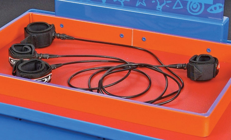 Two people wear interlinked handcuffs and solve how to disconnect without removing any handcuffs. An orange tray with four black velcro handcuffs that have cords between them.