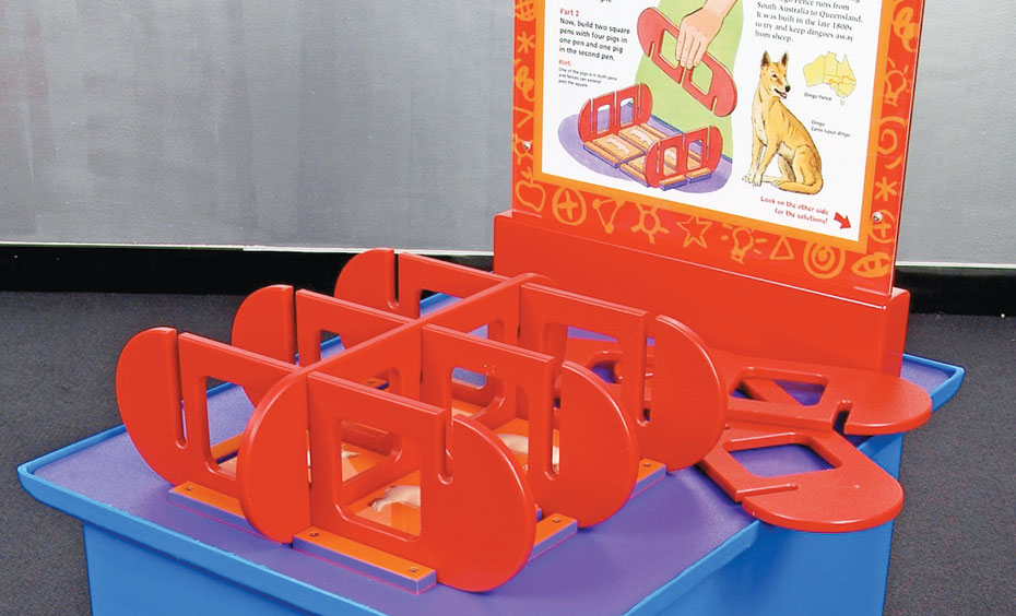 Use puzzle pieces to allocate areas and fences to different numbers of pigs. A purple exhibit table, with a white and orange information panel at the back. On top sits a series of red puzzles pieces that fit together to form enclosures.