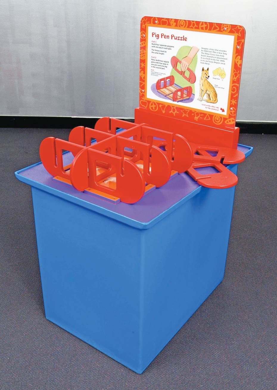 Dissecting space efficiently can create a greater number of enclosures. A purple exhibit table, with a white and orange information panel at the back. On top sits a series of red puzzles pieces that fit together to form enclosures.