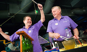 Two men in purple shirts standing in front of various science experiments.