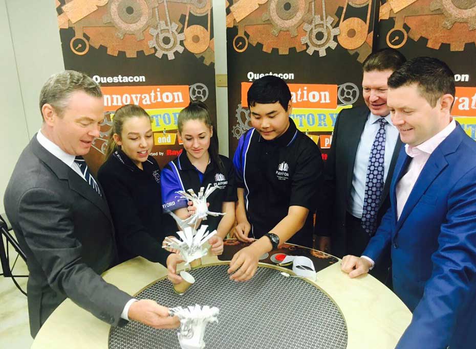Minister Pyne building flying cups over a wind table with three students and two men in suits