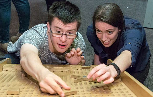 A woman helping a young man place pieces on a tilted peg board