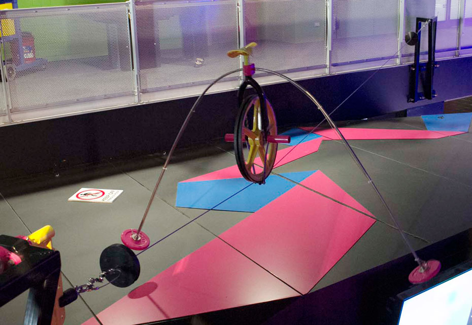 Why doesn't the wheel fall off the tightrope? A wheel sits on a cable tightrope, with two masses extending from the wheel so they hang below the cable tightrope