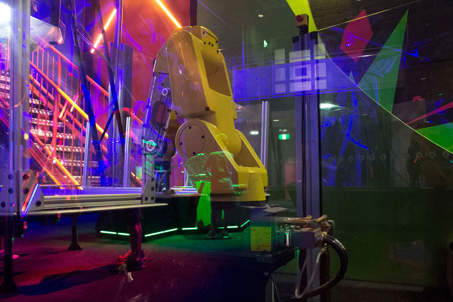 Robotic technology allows a mechanical arm to detect and respond to human actions in a challenging game of air hockey. a yellow robot arm with a hocky puck attached at the end of it's arm sitting on a blue air hockey table