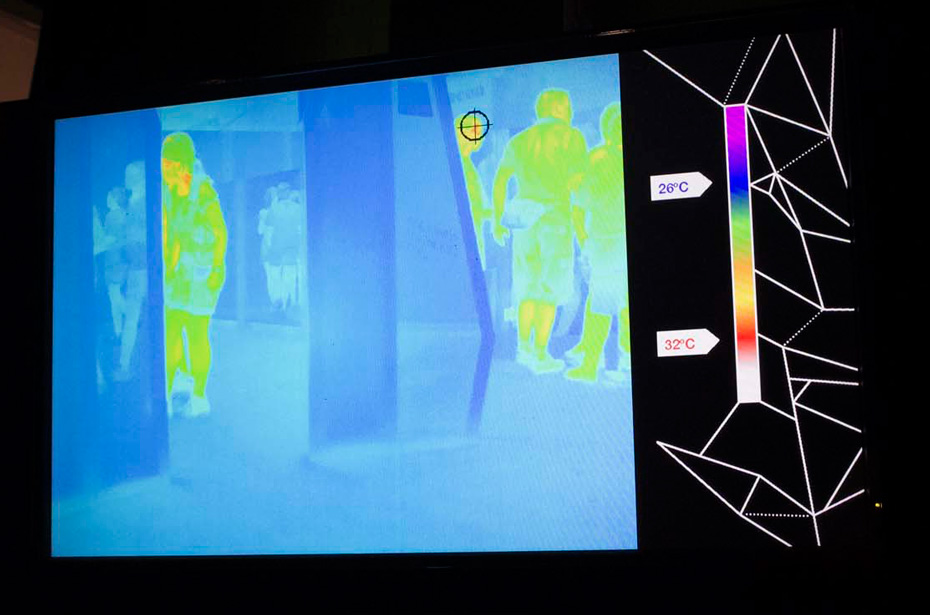 Thermal cameras detect human body heat and some materials are transparent to the naked eye, but do not allow detection of body heat by the thermal camera. A monitor showing the room in a blue colour, with green, yellow and red shapes of people standing out.