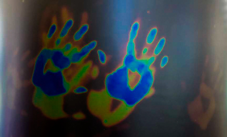 Thermocroic liquid crystals change colour when heated or cooled. Colourful blue, yellow and red handprints on a black background.
