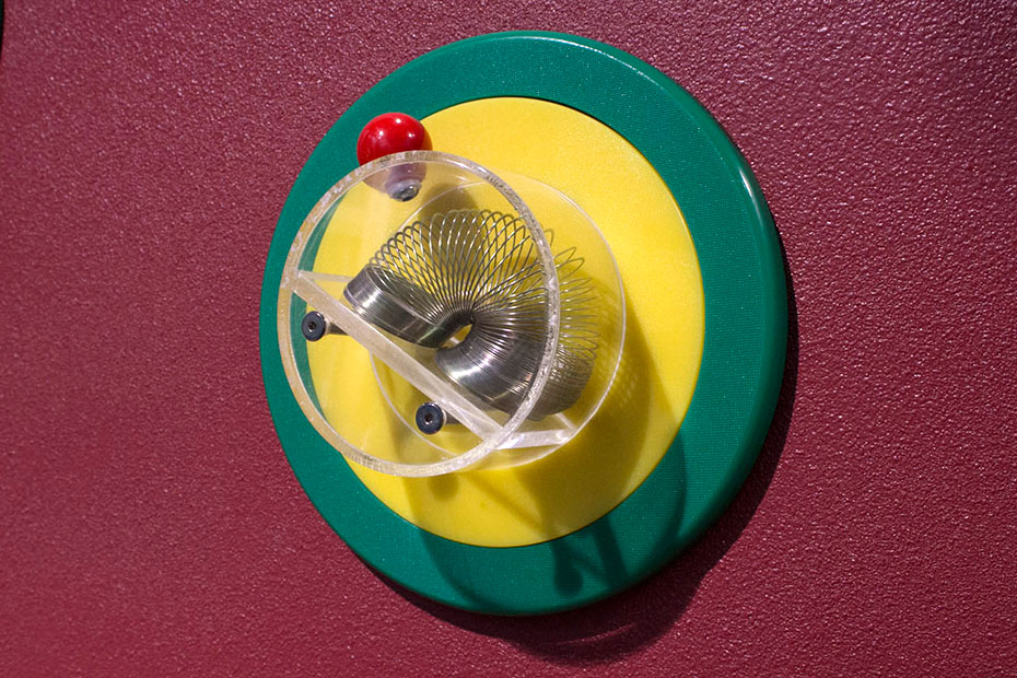 Explore different textures, sounds, lights and movements with your child. A slinky sitting in a perspex cup attached to a yellow and green disc, attached to a red wall