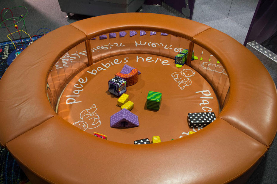 Toddlers may be at an intensely curious stage of talking and doing. You are probably familiar with the question “What’s that?” A round padded tan coloured play area with mirrors in the inside wall and assortment of soft toys in the centre area. The words "Place babies here" is written on the padded floor.