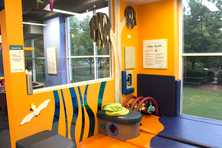 A special space for babies and their carers. A brightly coloured room of yellow, blue and purple, with windows looking to outside garens, and soft play matts and baby toys on the ground.