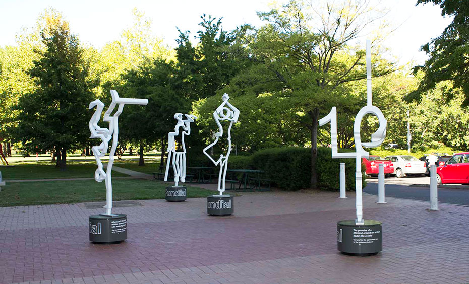 Walk around each of the four sculptures to view their shadows and gauge which shadow represents a number that is closest to the time of day. Four white steel outline scupltures of people on a paved area with gardens in the background.