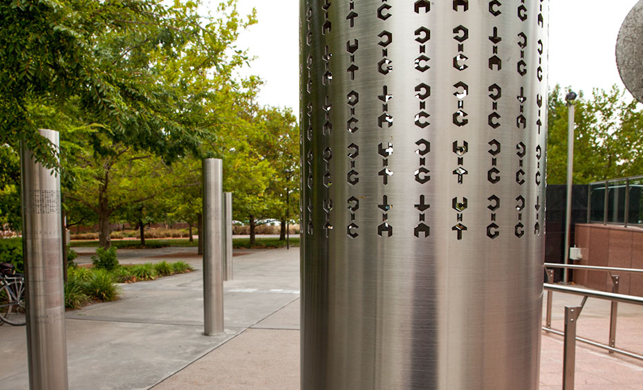 Hidden messages can be communicated using encryption or code. Four stainless steel vertical poles about 2 metres in height are spaced apart and embedded into a concrete and paved garden area. On each of the poles are laser cut out cryptographic symbols.