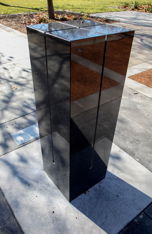 Knock around the top and sides of the pillar and listen carefully for the subtle sounds you create. A rectangular black granite pilar about 1500 milimeters heigh, with for slits running from across the top to three quarters of the way down the sides. The pilar sits on concrete and is located in a garden environment.