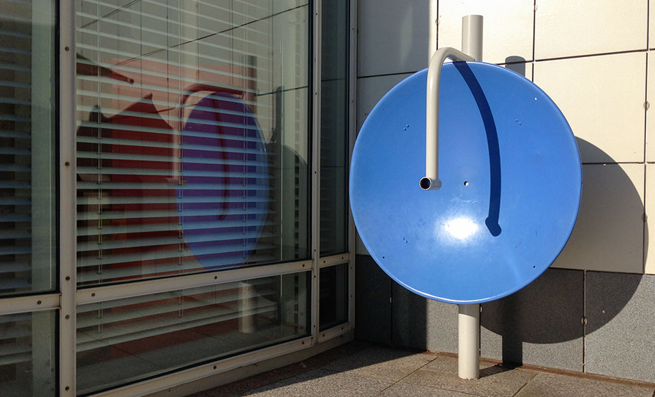 Large, flat dishes reflect sound waves to certain points. A large blue concave vertical dish sits in the corner with a large window to the left and a white wall to the right.