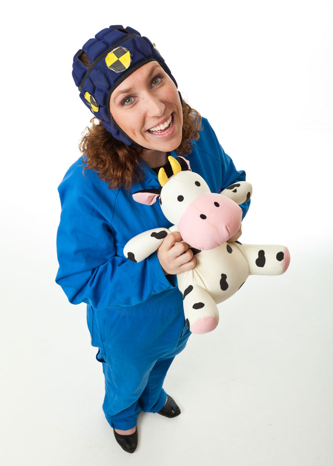 A woman in overalls, wearing a safely crash cap and holding a plush toy cow.
