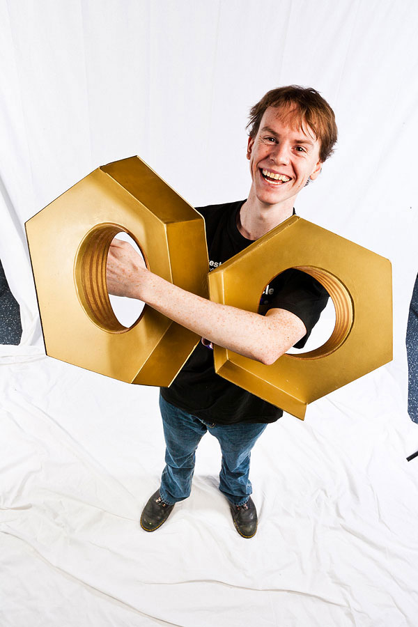 A man smiling and holding two over sized model hex nuts through his left arm.