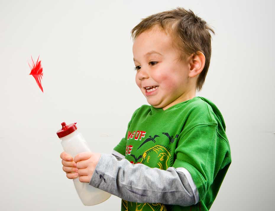 A young boy smiling with a plastic drink bottle in his hands.