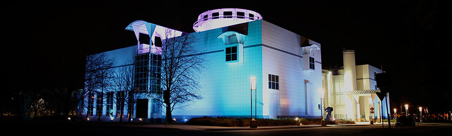 A night time photo of a large building which has lights shining up upon its outside walls.