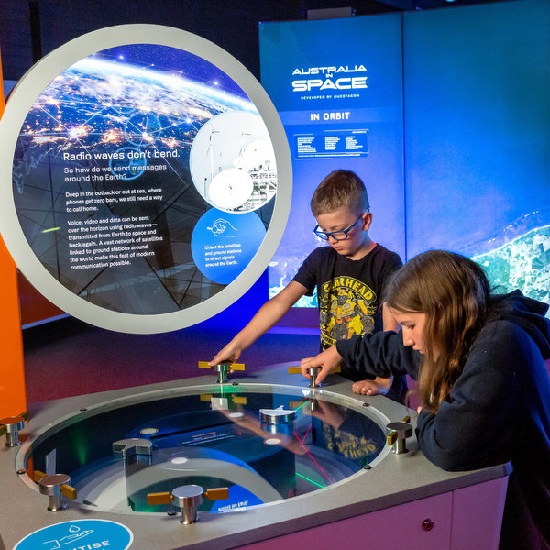 Visitors engaging with an interactive exhibit at the Australia in Space exhibition Visitors engaging with an exhibit at the Australia in Space exhibition at Questacon