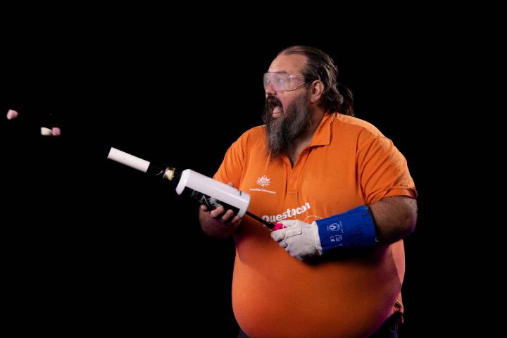 Man in orange shirt shoots marshmallow gun into air