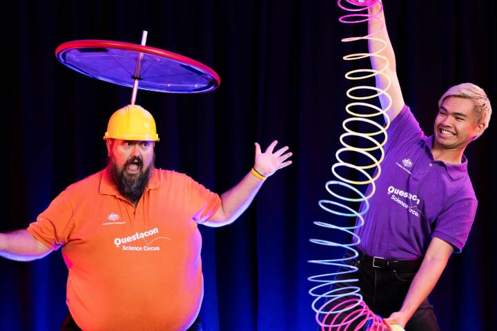 A man with a spinning top on his head and another with a giant slinky