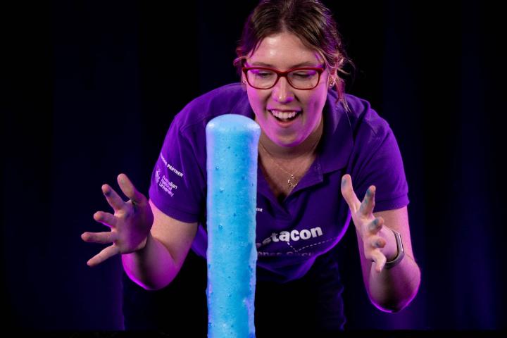Woman watches as blue foam bubbles out of tall flask