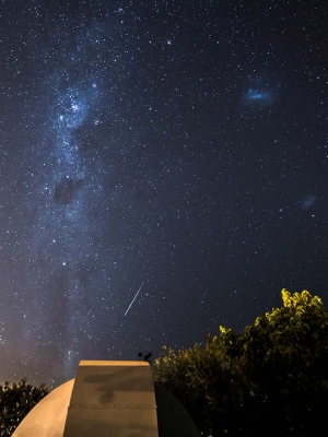 A large telescope pointed at the night sky and the milky way with a shooting star.